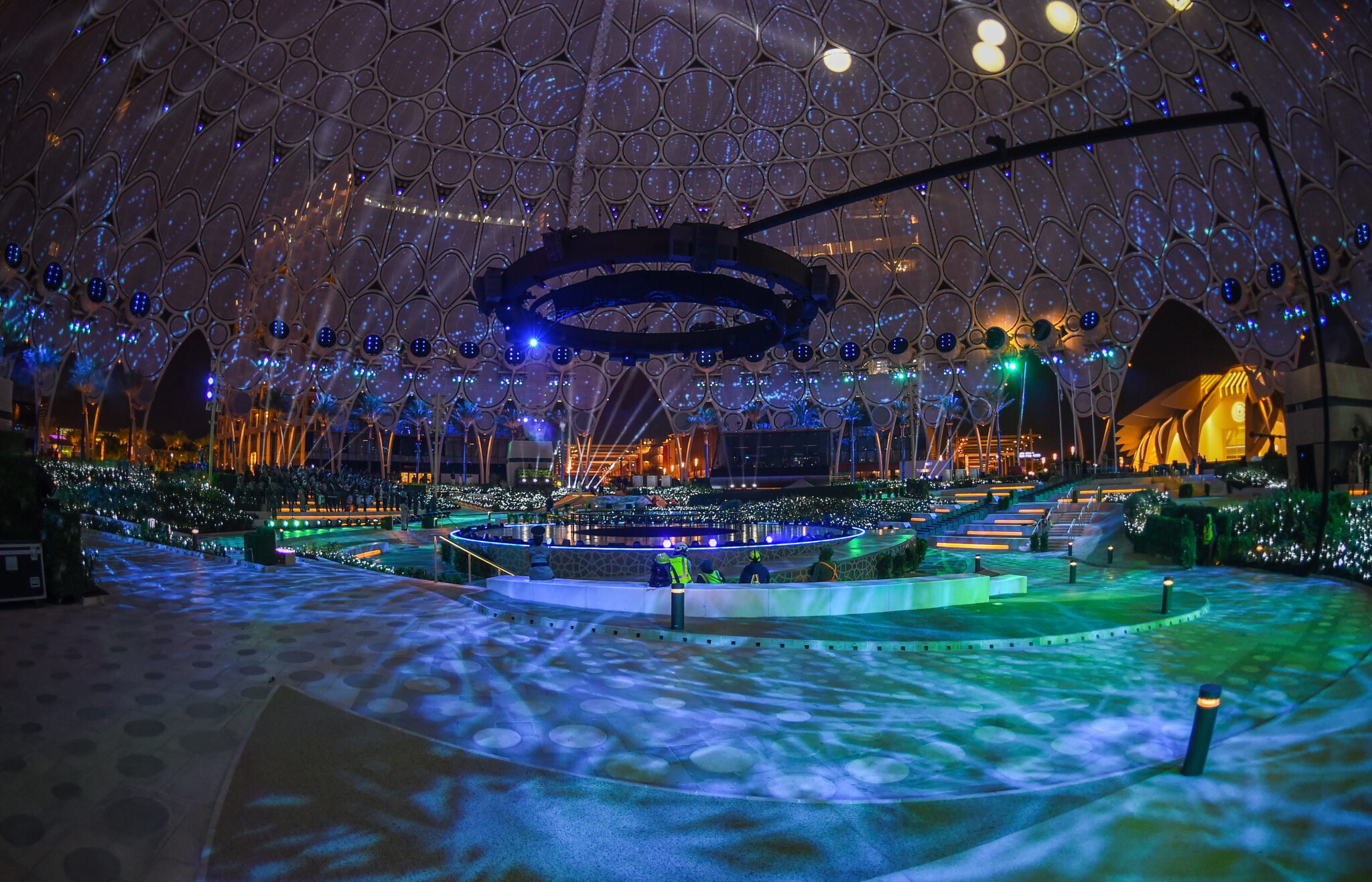 A darkened arena floor lit in blue and green, with projected water imagery spreading across the ground and the dome above.