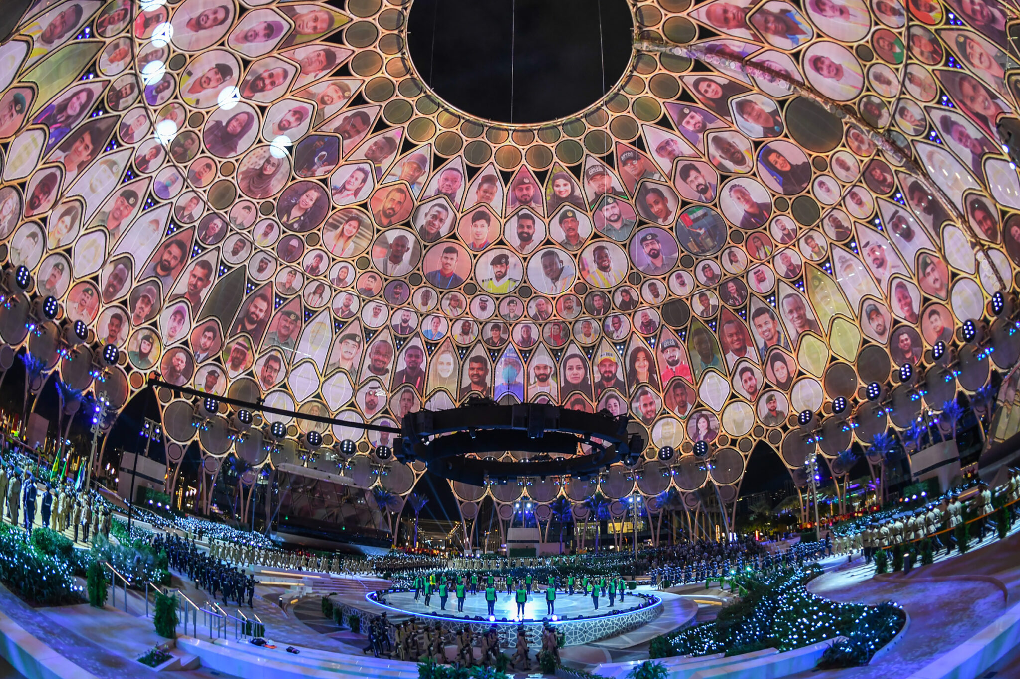A domed arena ceiling filled edge to edge with warm pink and coral projected patterns, seen from the floor below.