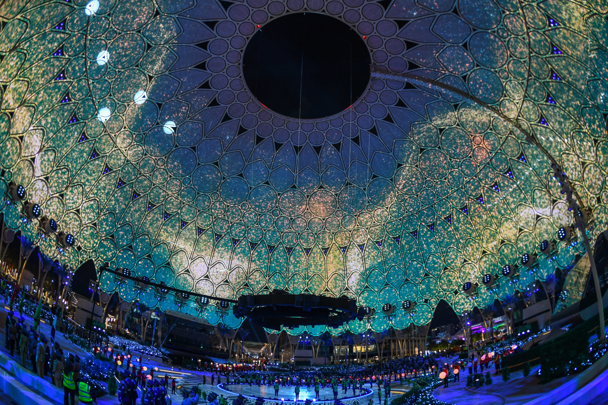 The inside of a large dome covered in teal and green organic projected patterns, with a dark circular opening at its centre.