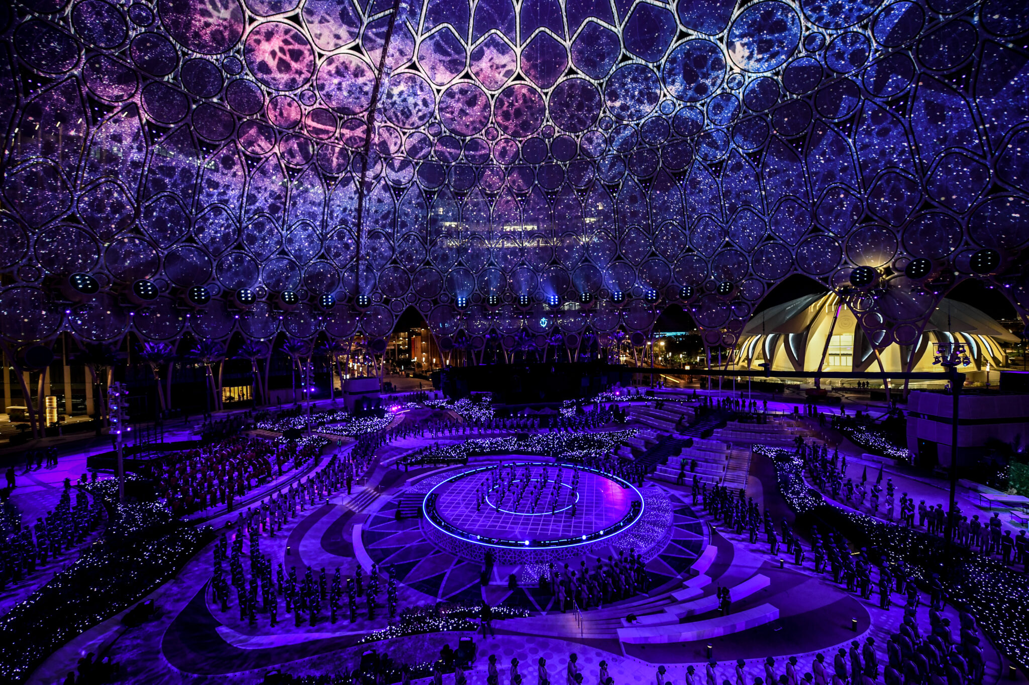 The interior of a dome lit in deep purple and violet projections, with a circular opening at the apex and a lit floor below.
