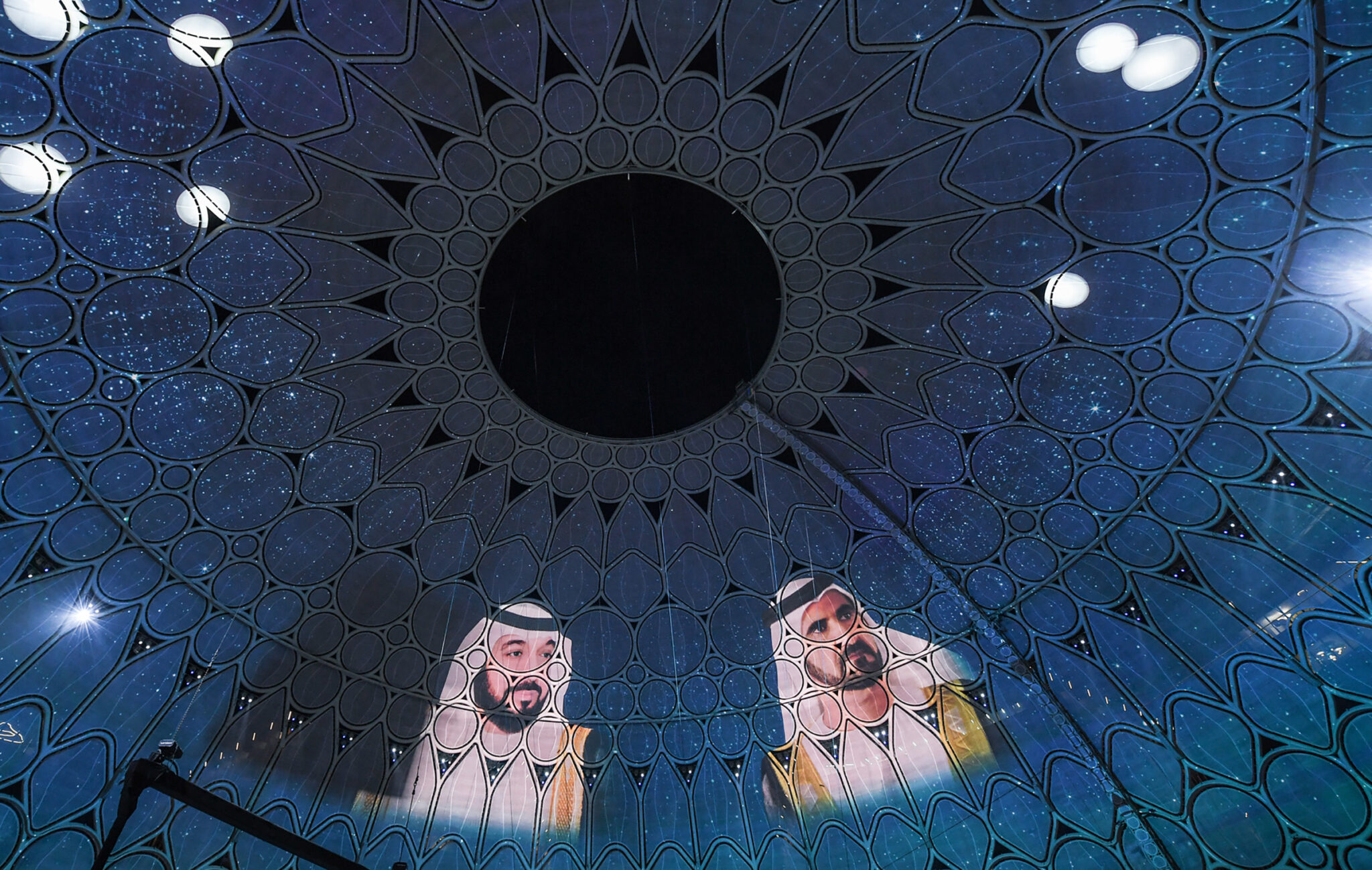The inside of a large dome covered in teal and green organic projected patterns, with a dark circular opening at its centre.