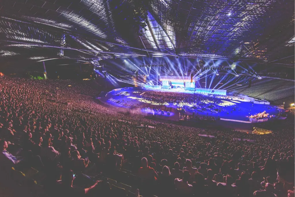 Packed stadium with a large audience watching a live performance at the BMW Festival, illuminated by vibrant stage lights and effects. Battle Royal Studios