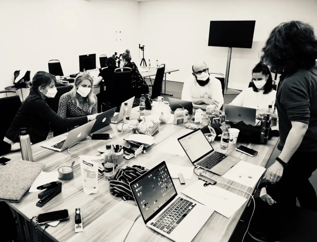 A group of people wearing masks work together in a meeting room, surrounded by laptops and office supplies. Battle Royal Studios