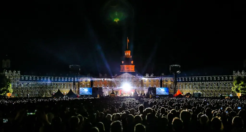 A large crowd watches a nighttime event with light projections on a grand building. BattleRoyalStudios