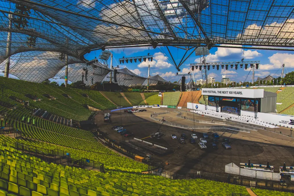 Empty stadium during the setup for the BMW Festival, with the stage and cars in place under a clear blue sky. Battle Royal Studios