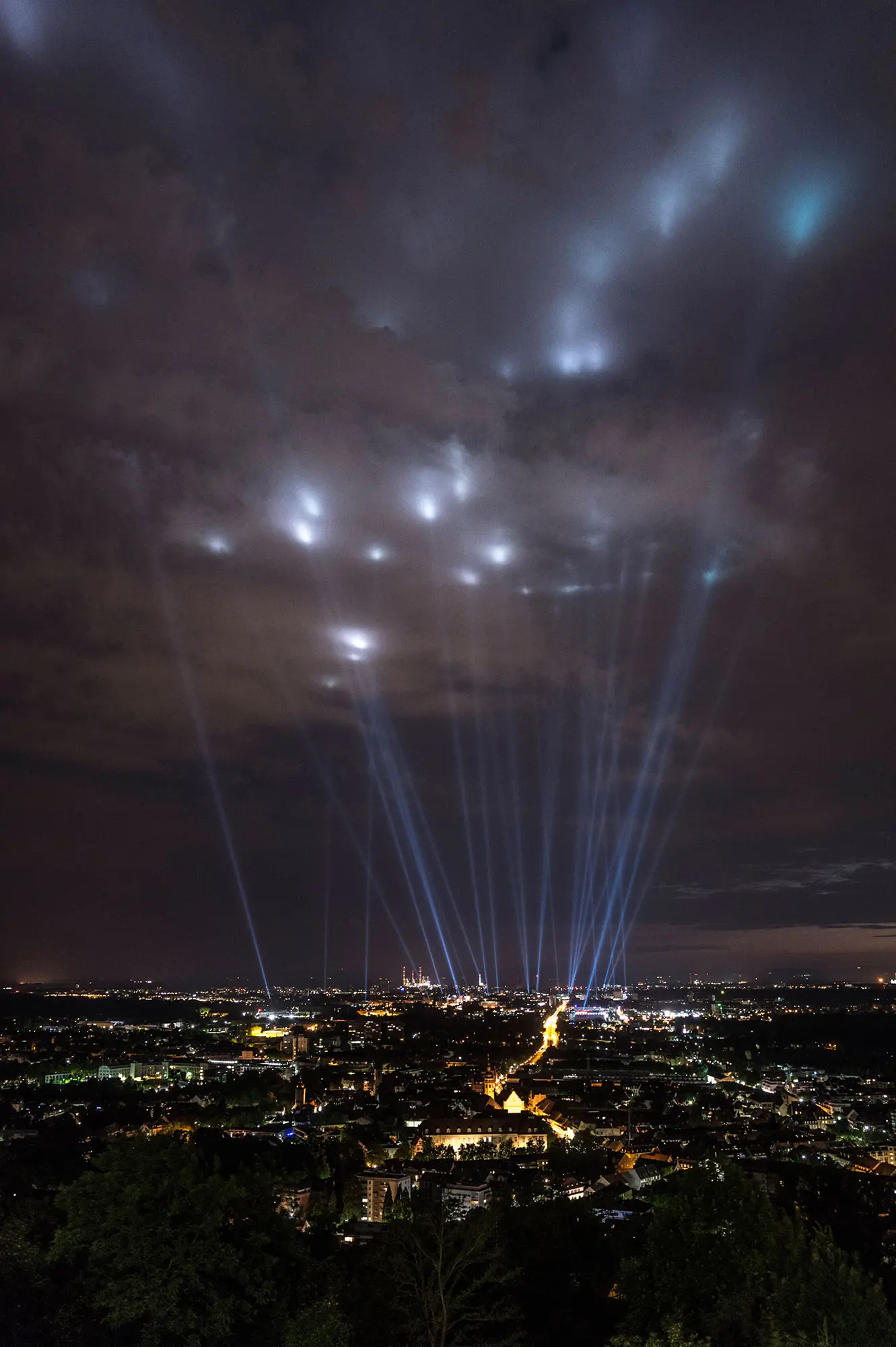 A night view of a city skyline with bright beams of light projecting into the cloudy sky. Battle Royal Studios