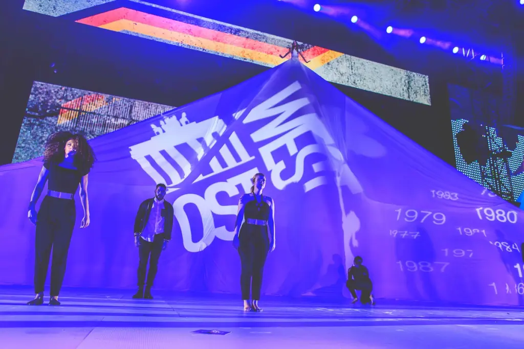 Performers on stage in front of a large projected image, illuminated in blue light during a dramatic moment at the BMW Festival. Battle Royal Studios