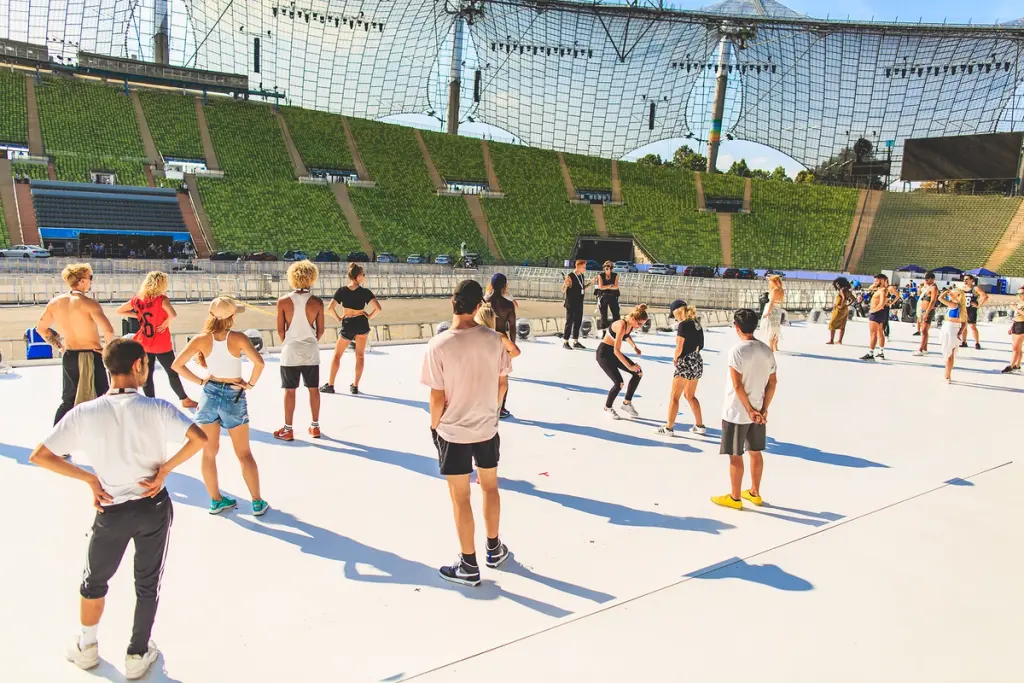 Performers rehearsing on a large stage in an empty stadium during preparations for the BMW Festival. Battle Royal Studios