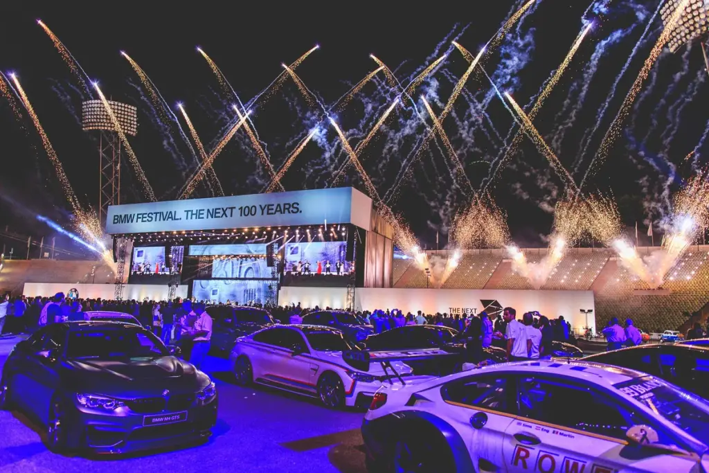 Fireworks lighting up the sky above the BMW Festival stage, with a display of cars and a crowd gathered below. Battle Royal Studios