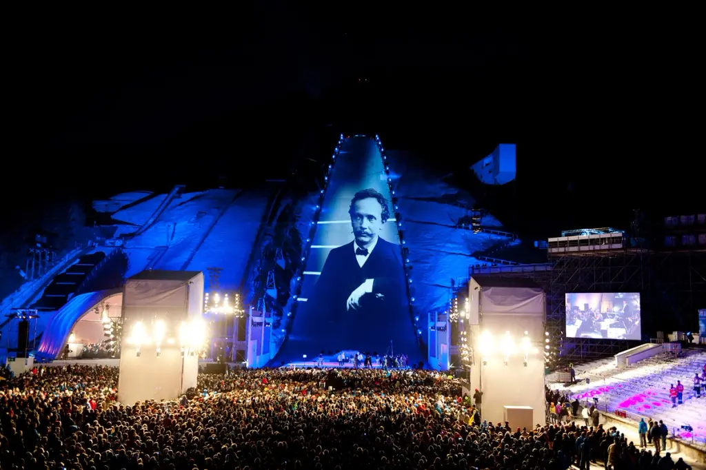 Large outdoor event with a giant projection of a historical figure on a ski jump, illuminated in blue. BattleRoyalStudios