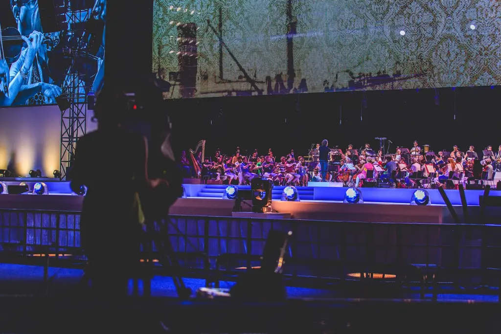 Orchestra performing on stage with a large screen displaying close-up images of musicians at the BMW Festival. Battle Royal Studios