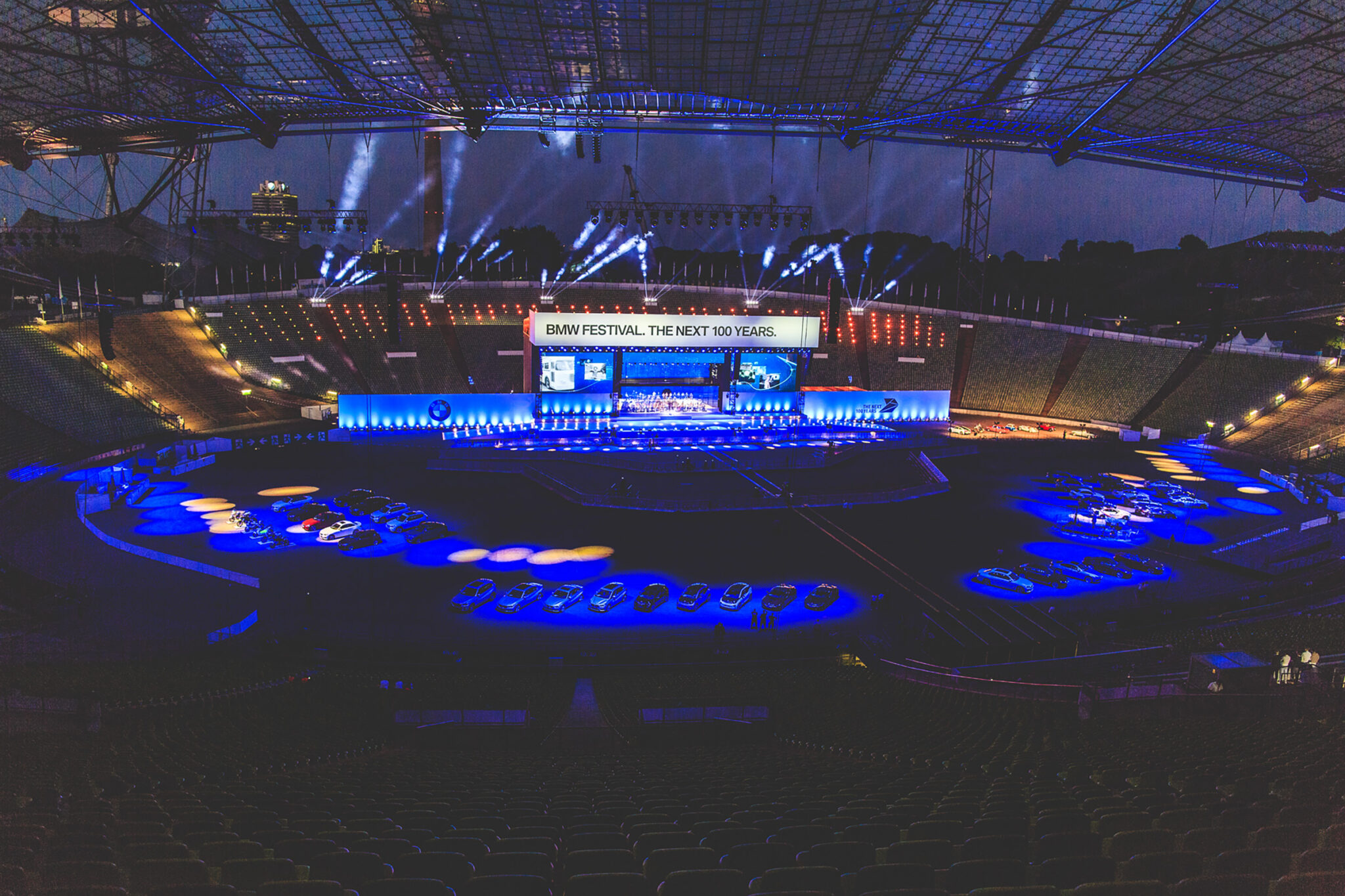 Panoramic view of the BMW Festival stage with dramatic lighting, fireworks, and cars on display in a stadium setting. Battle Royal Studios
