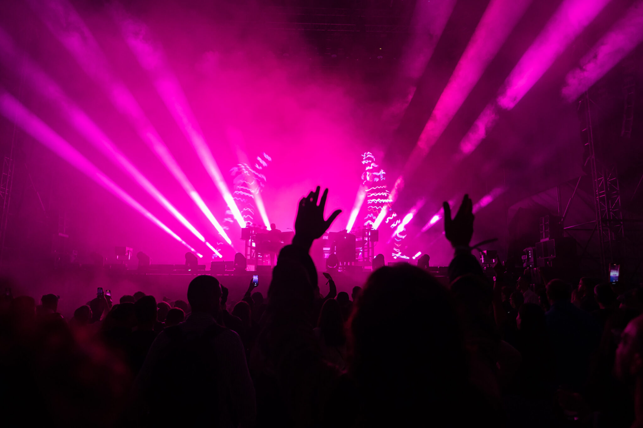 Pink light beams fan out over a dark crowd raising their hands in front of the stage.