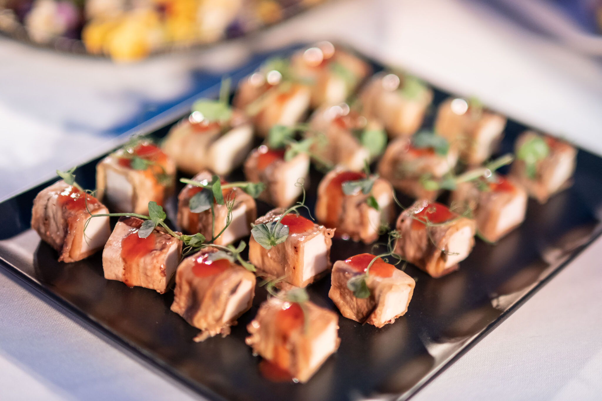 A tray of skewered bite-sized pieces of grilled meat with sauce and herbs.