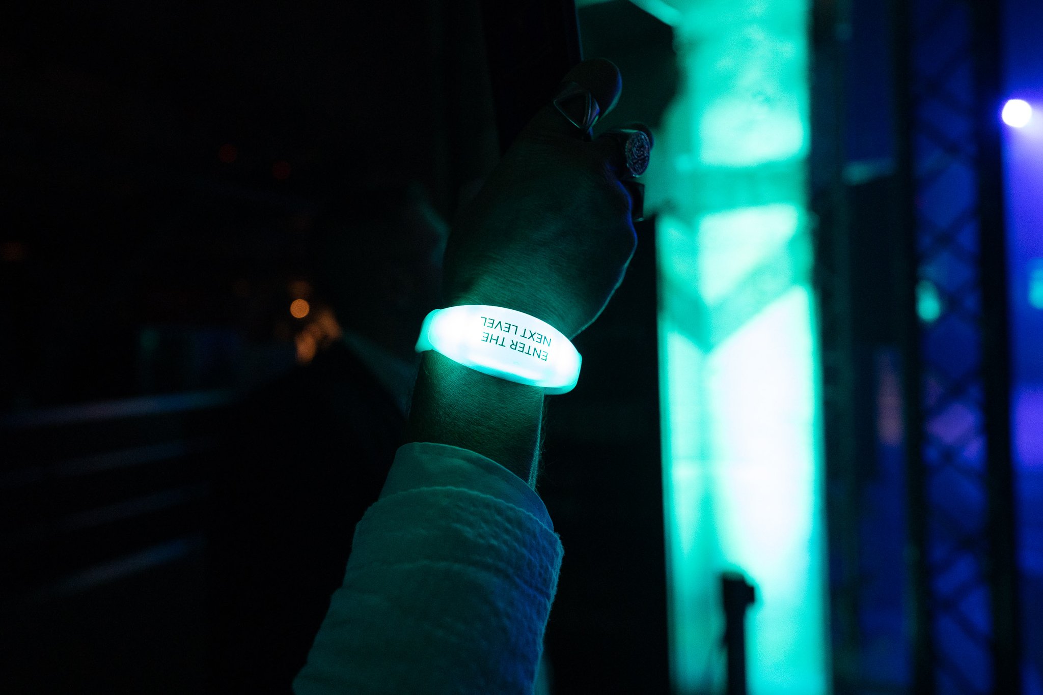 A glowing white wristband on a guest's wrist in a dark space lit by teal light.