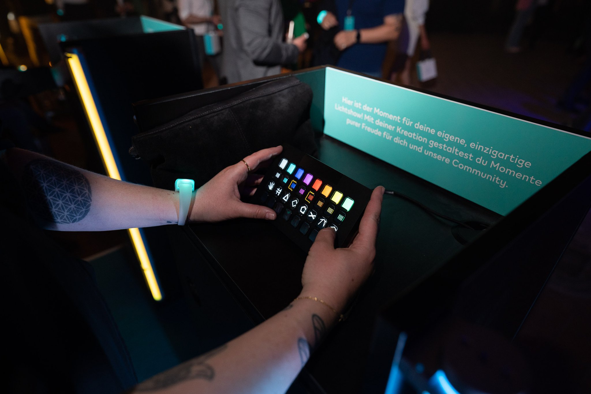Two hands hold a small device with colourful buttons over a dark table with a lit text panel.