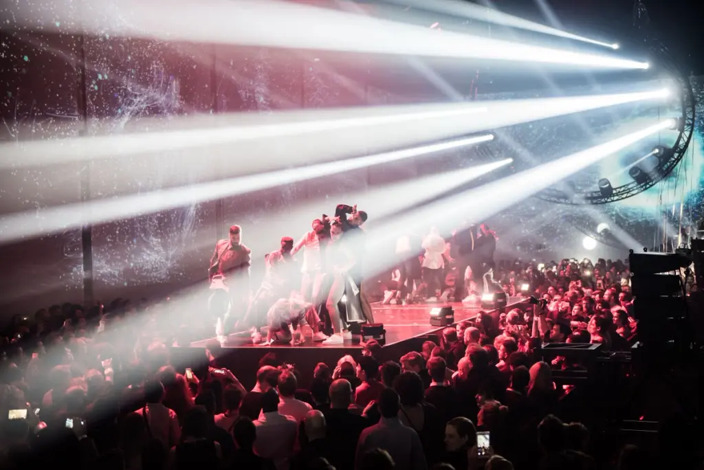 Performers on stage illuminated by powerful beams of light with an audience watching. Battle Royal Studios