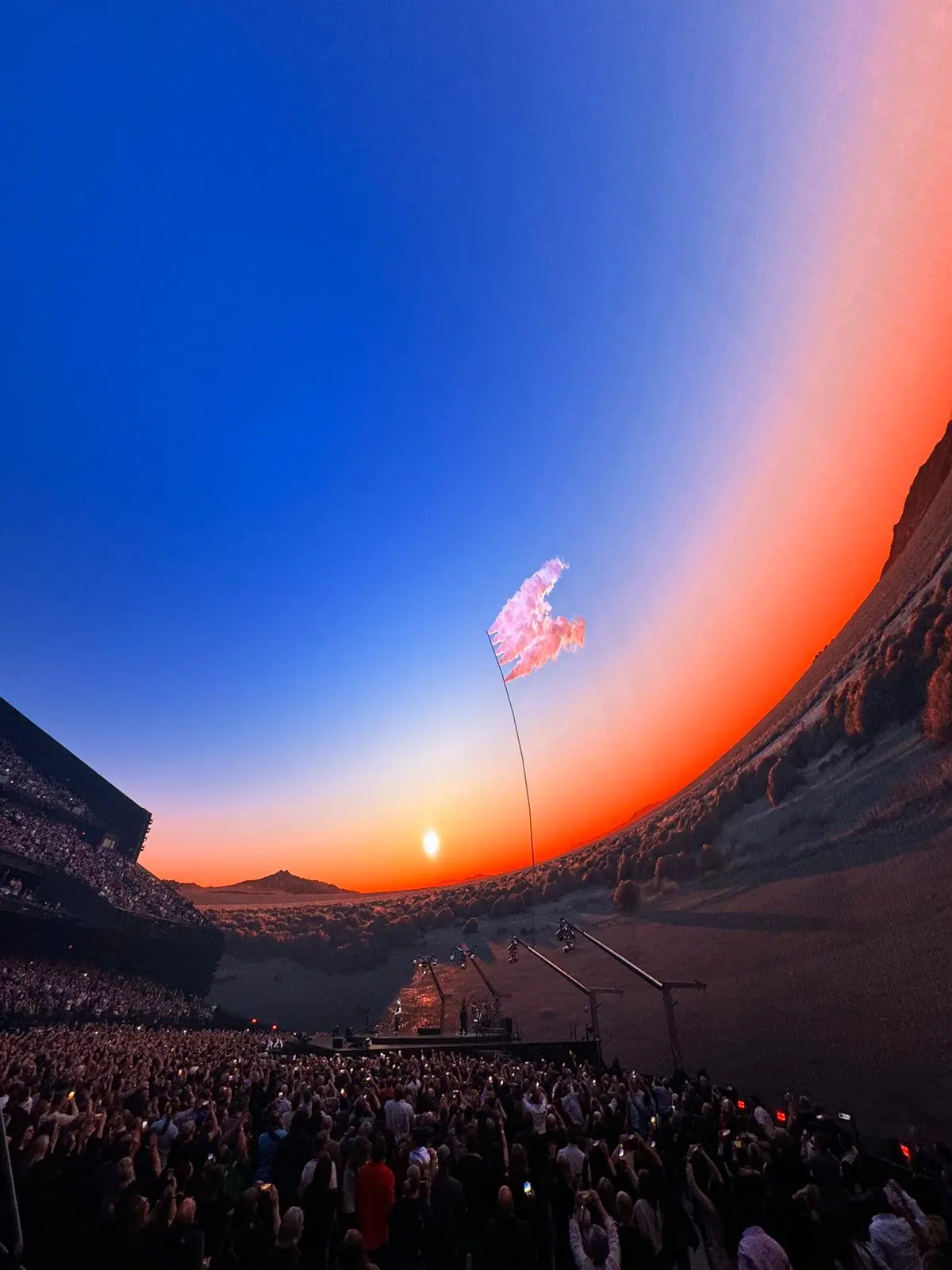 A concert audience watches a sunset landscape projected on a massive dome, with a flag waving in the scene. Battle Royal Studios