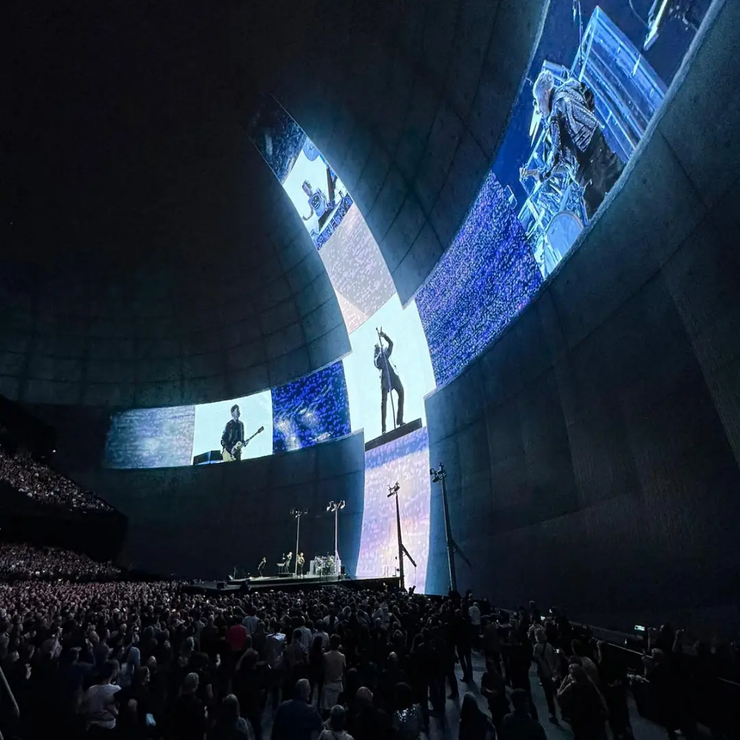 A large crowd watches a concert under a dome with massive screens displaying live footage of the performers on stage. Battle Royal Studios