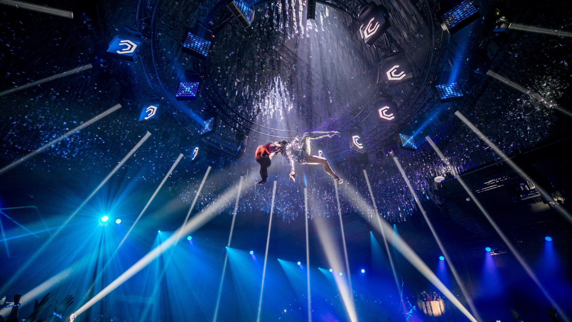 Aerial performers suspended in mid-air during a dramatic light show at a Battle Royal Studios event, with an audience below