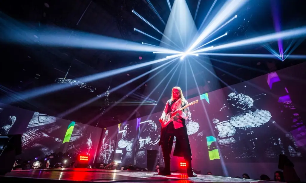 Guitarist performing on stage with dramatic lighting and visual projections at a Battle