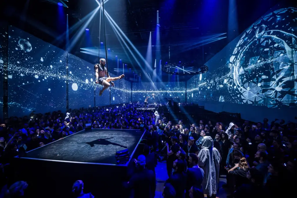 Aerial performer suspended above a stage with a crowd below, surrounded by immersive digital projections. Battle Royal Studios