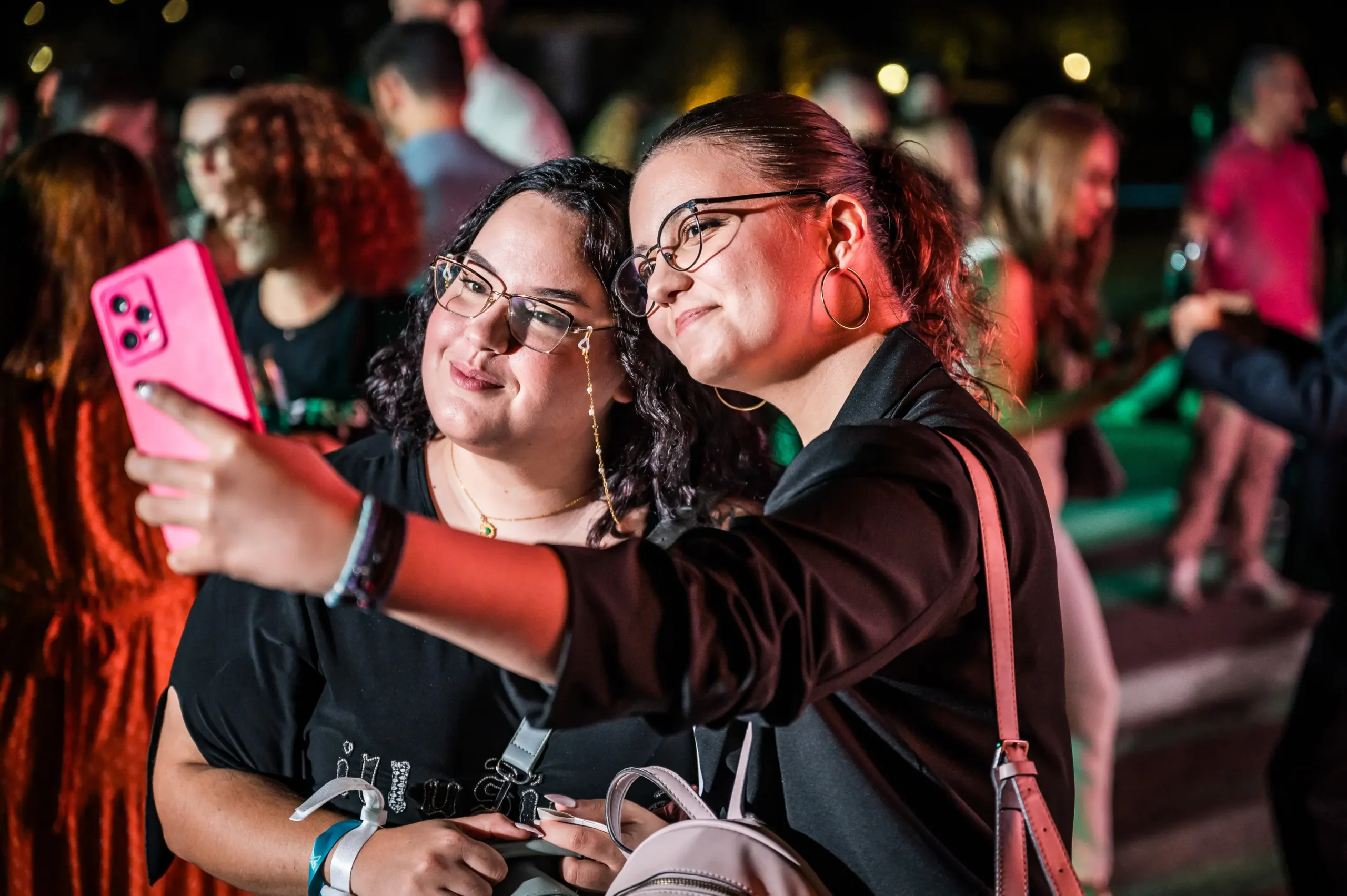 Two women smiling and taking a selfie together at an event, surrounded by other attendees. BattleRoyalStudios