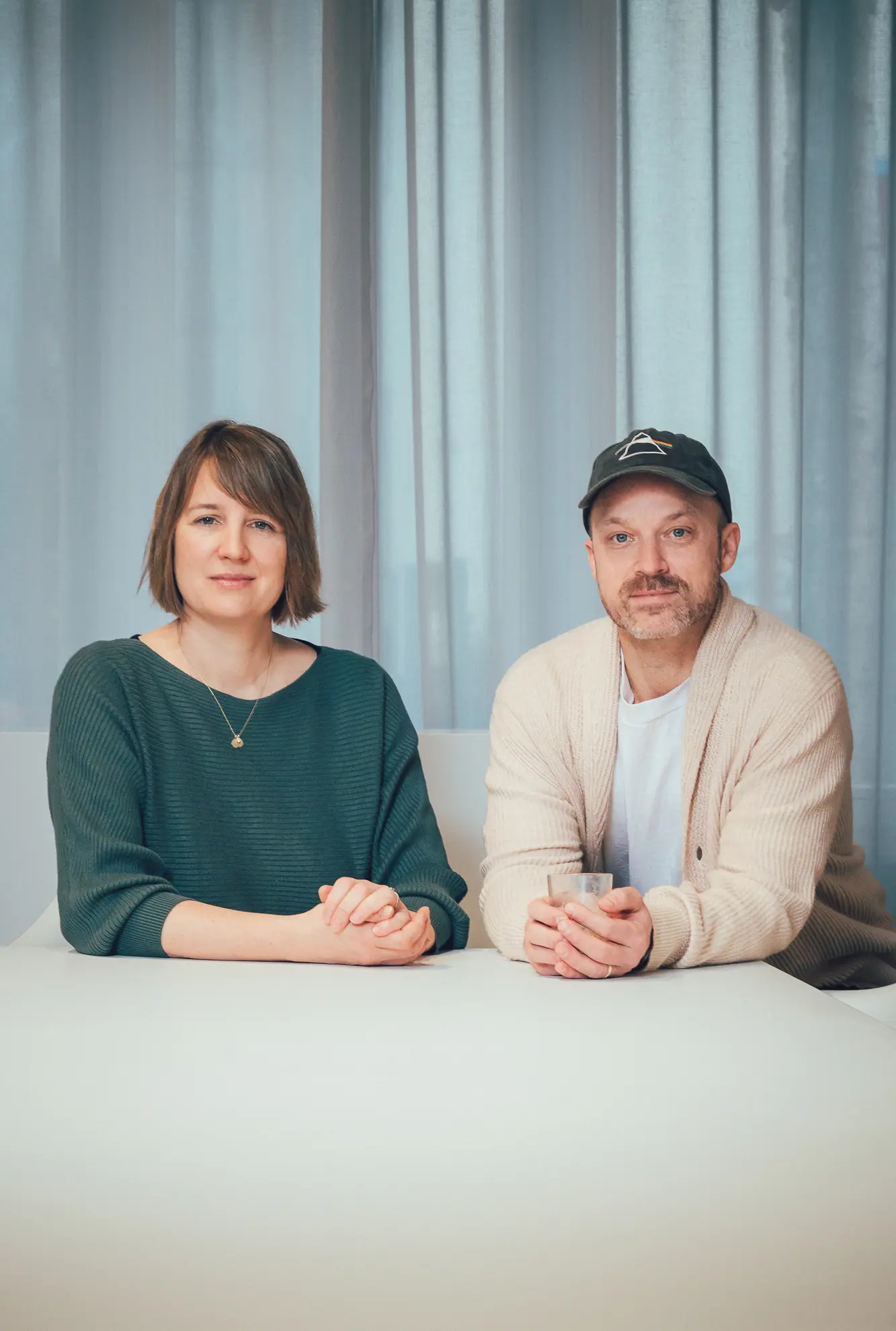 A woman and a man sitting together at a white table in front of a curtain