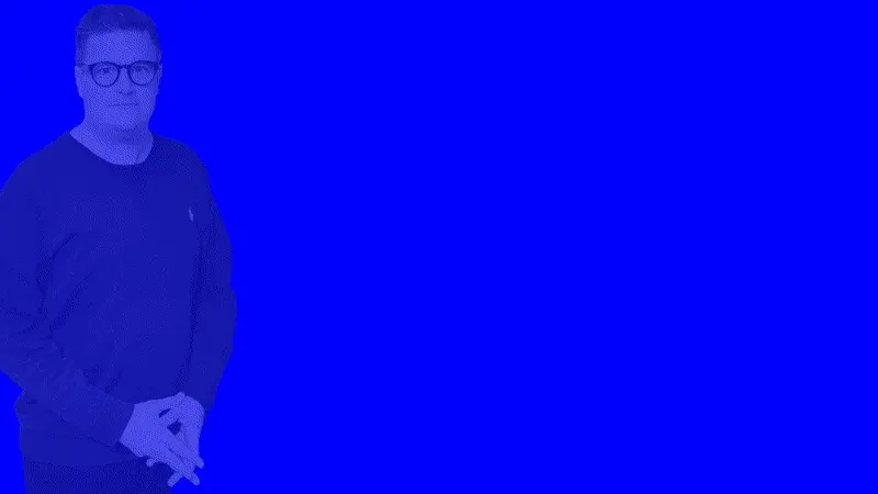 A man in a dark sweater standing in front of a bright blue background