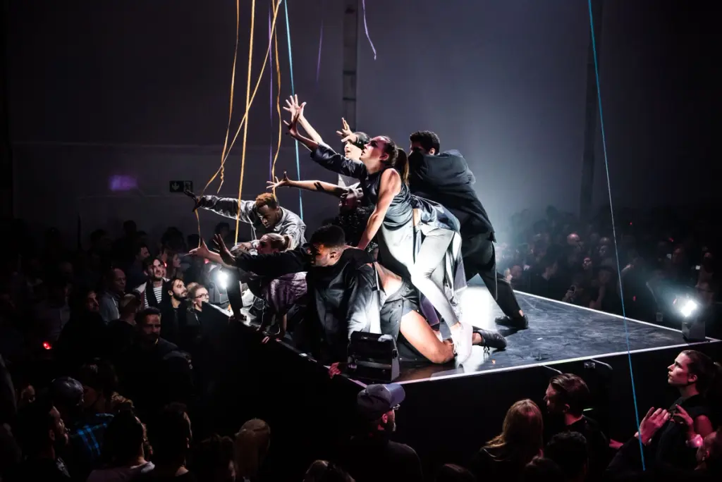 Performers in a dynamic pose on stage reaching towards the audience. Battle Royal Studios