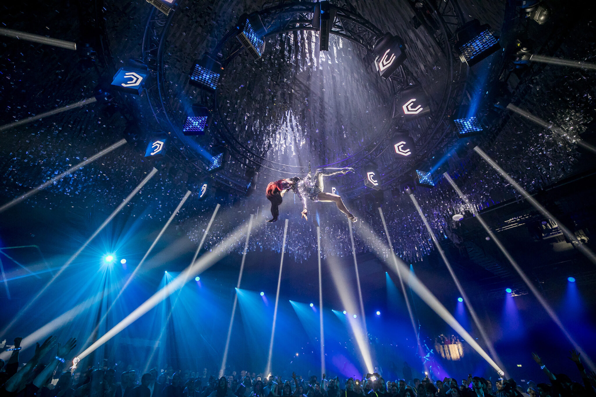 Aerial performers suspended in mid-air during a dramatic light show at a Battle Royal Studios event, with an audience below