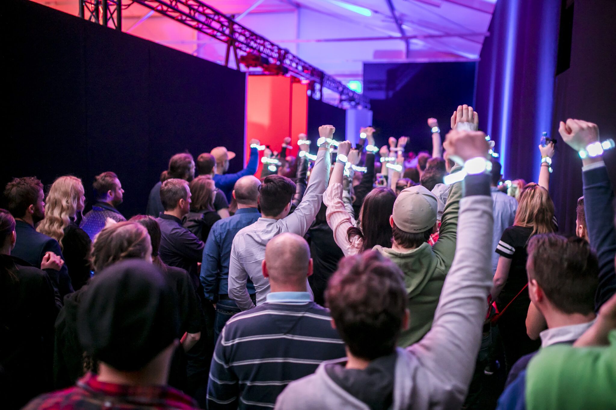 A crowd raising hands with glowing wristbands in a dimly lit venue, creating a vibrant atmosphere. Battle Royal Studios