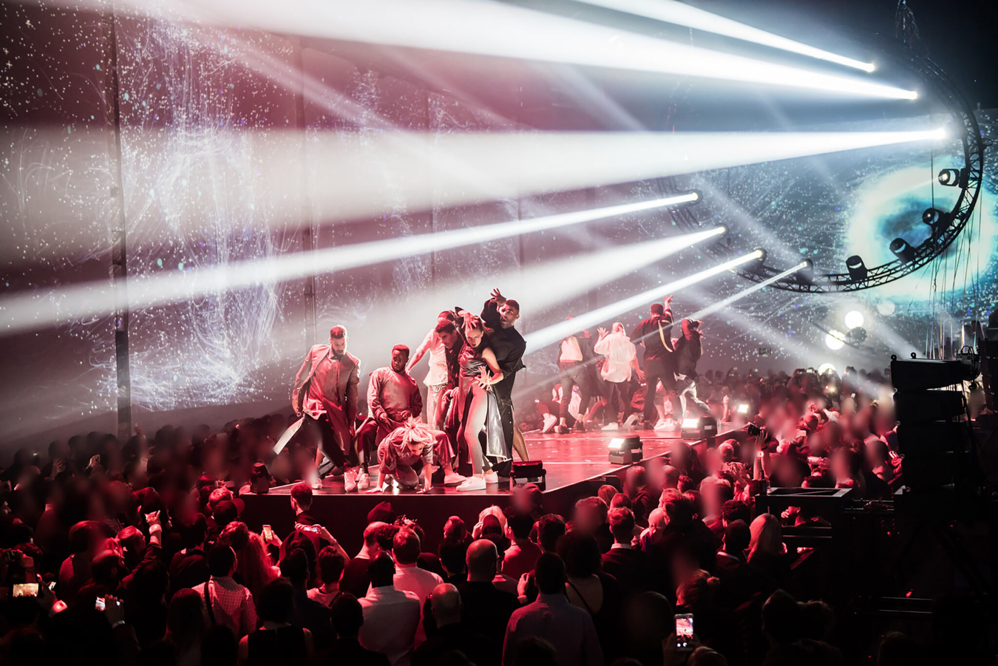 Performers on stage illuminated by powerful beams of light with an audience watching. Battle Royal Studios