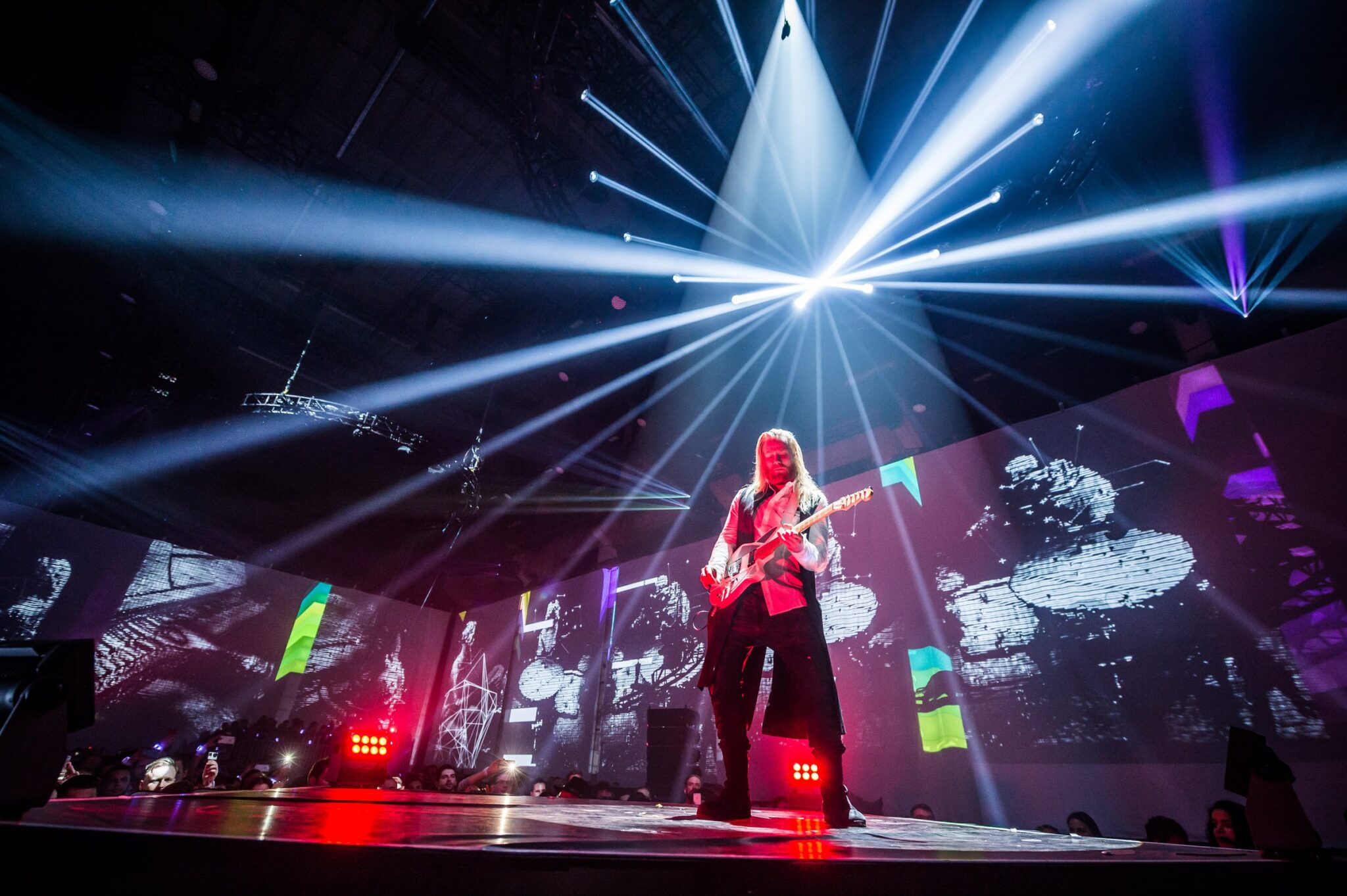 Guitarist performing on stage with dramatic lighting and visual projections at a Battle Royal Studios event