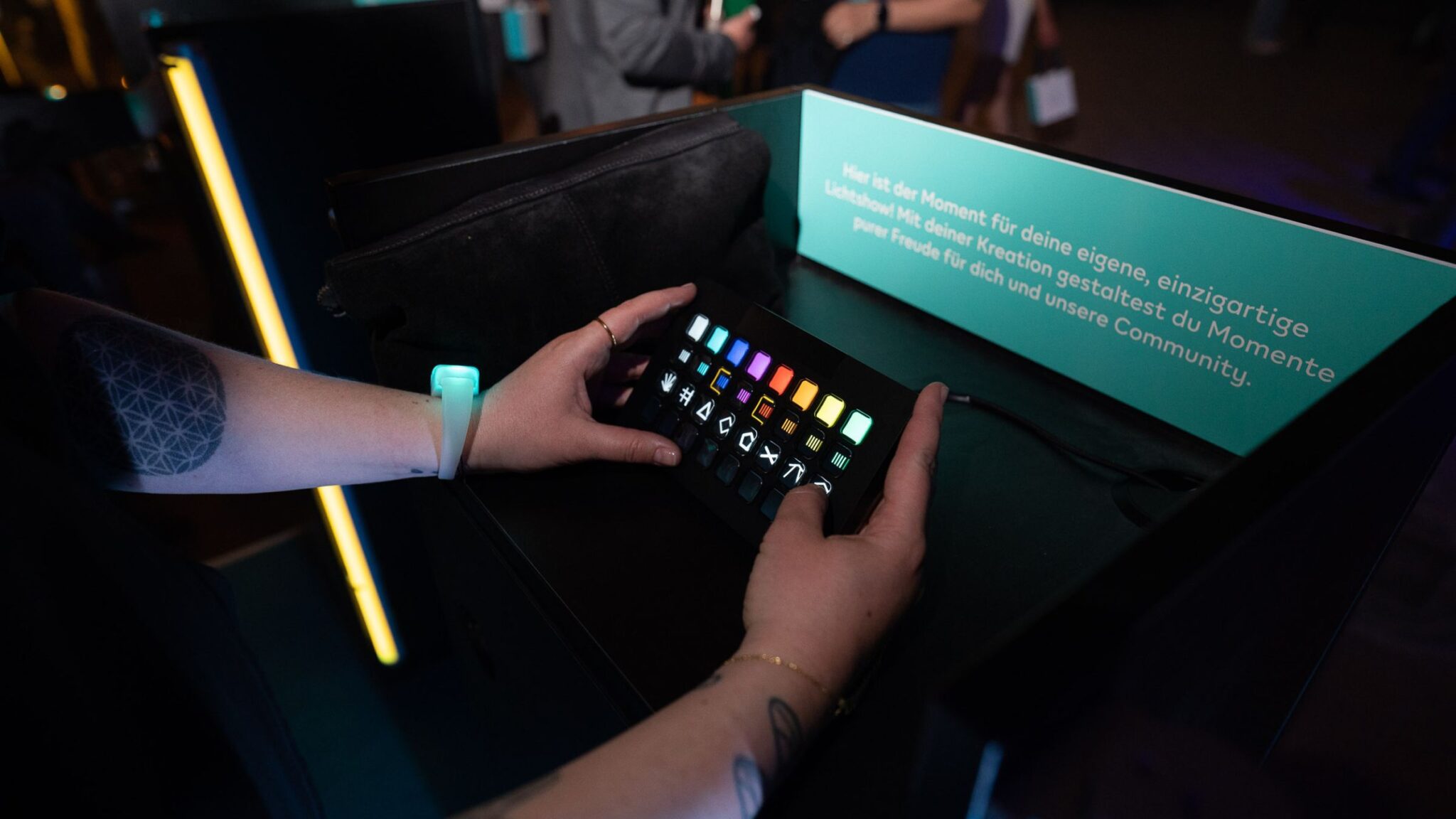 A person interacting with a small control panel featuring colorful illuminated buttons, wearing a glowing wristband, in a dimly lit environment. Battle Royal Studios