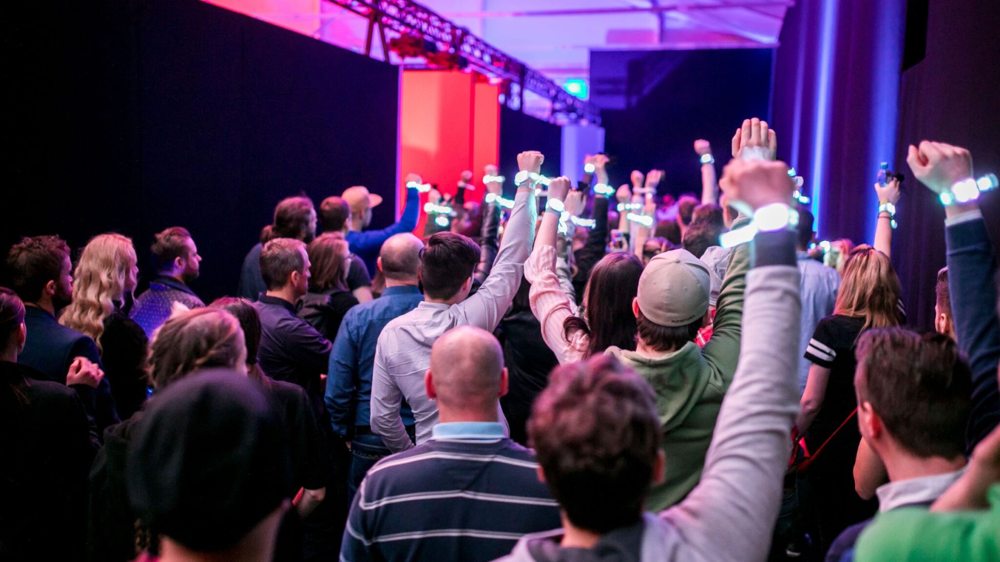 Audience members raising their arms with glowing wristbands, in a dimly lit indoor event space. Battle Royal Studios.