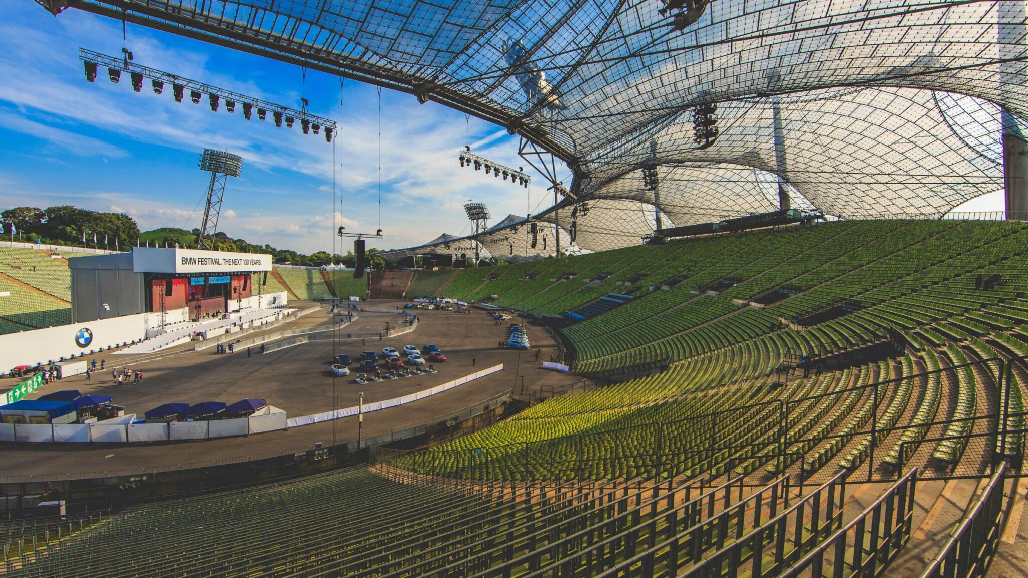 Empty outdoor stadium with a large stage setup for the BMW Festival, featuring a transparent canopy and green seating areas. Battle Royal Studios.