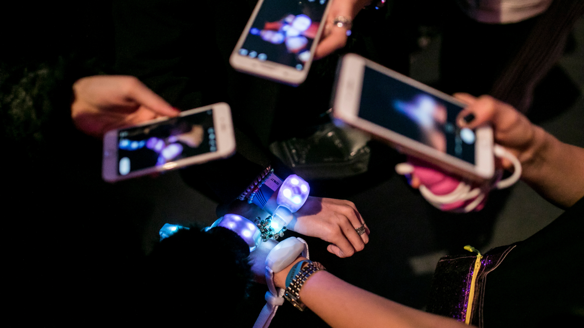 Close-up of several glowing wristbands being photographed by multiple smartphones, capturing the interactive experience. Battle Royal Studios