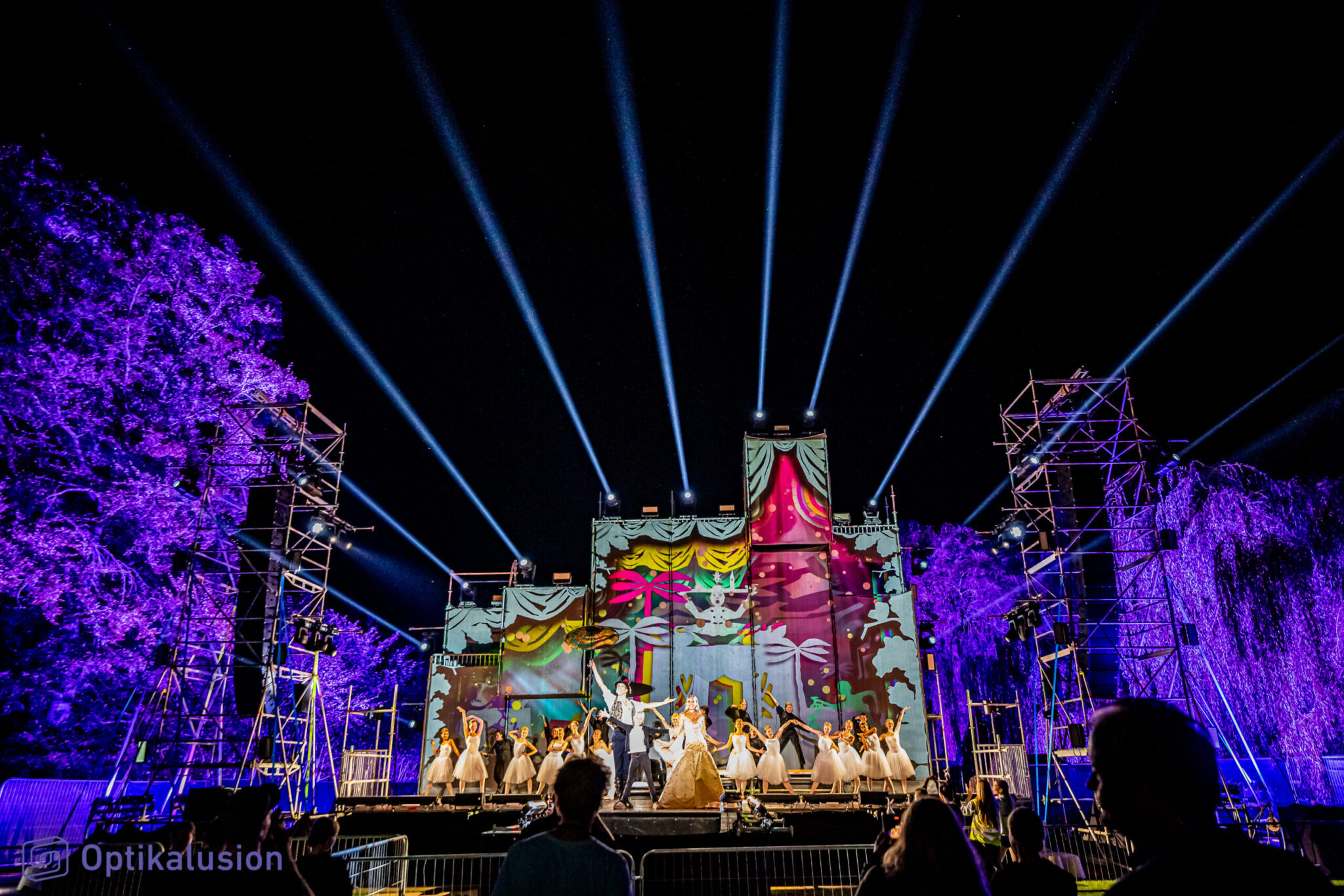 A colorful stage show with dancers, vibrant lighting, and beams in the night sky. Battle Royal Studios