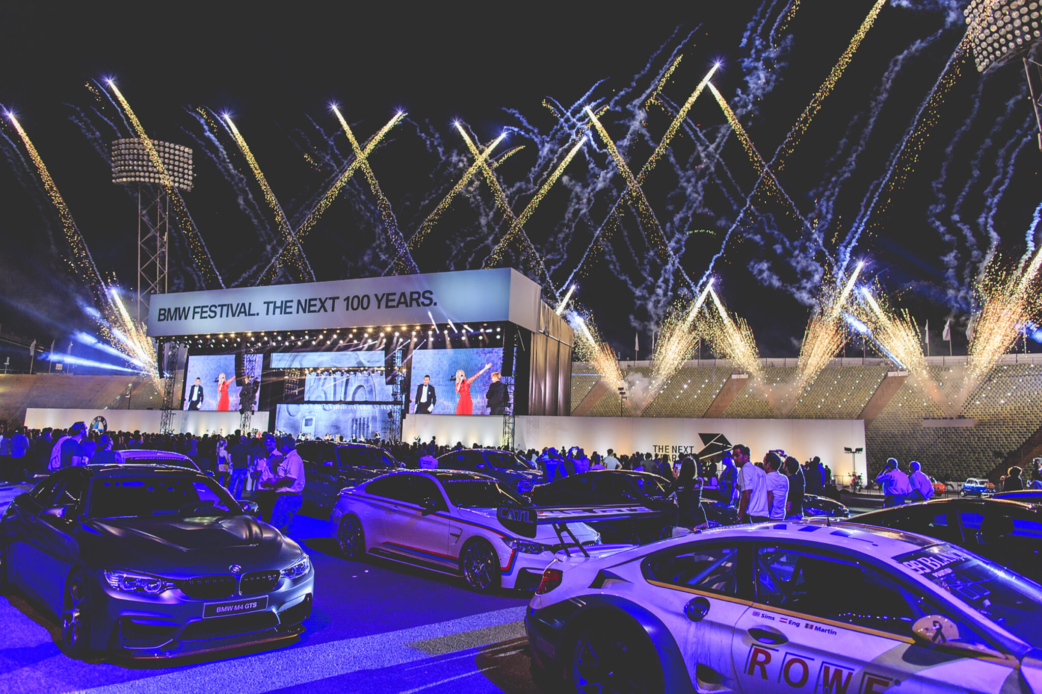 Fireworks lighting up the sky above the BMW Festival stage, with a display of cars and a crowd gathered below. Battle Royal Studios