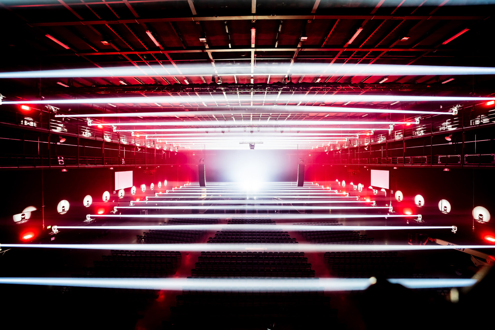 A long corridor of crossed red and white light beams converging towards a bright point in the distance, forming a tunnel of light.