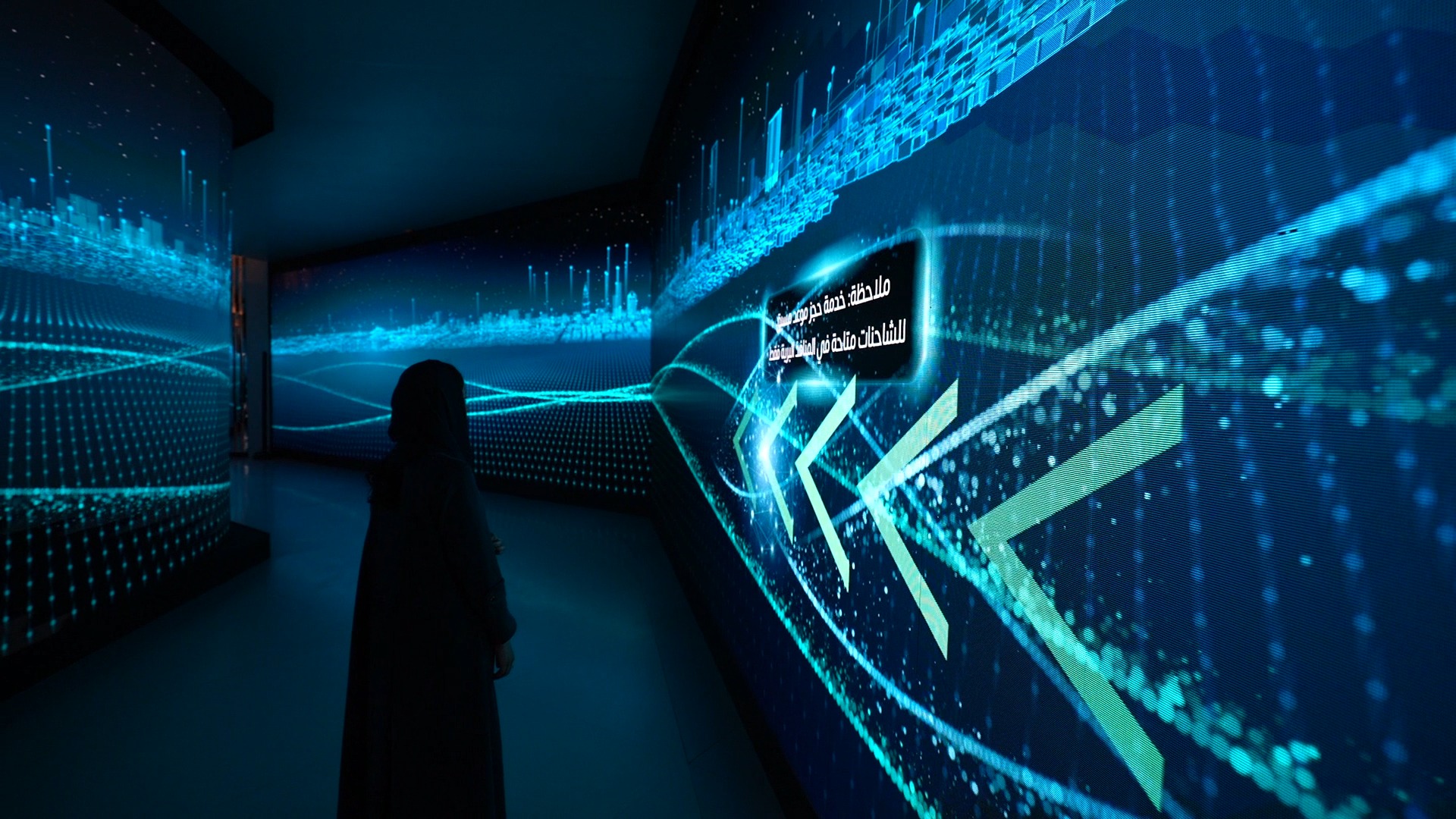 A visitor stands in a dark corridor lined with LED walls showing flowing blue light lines and large green arrows.