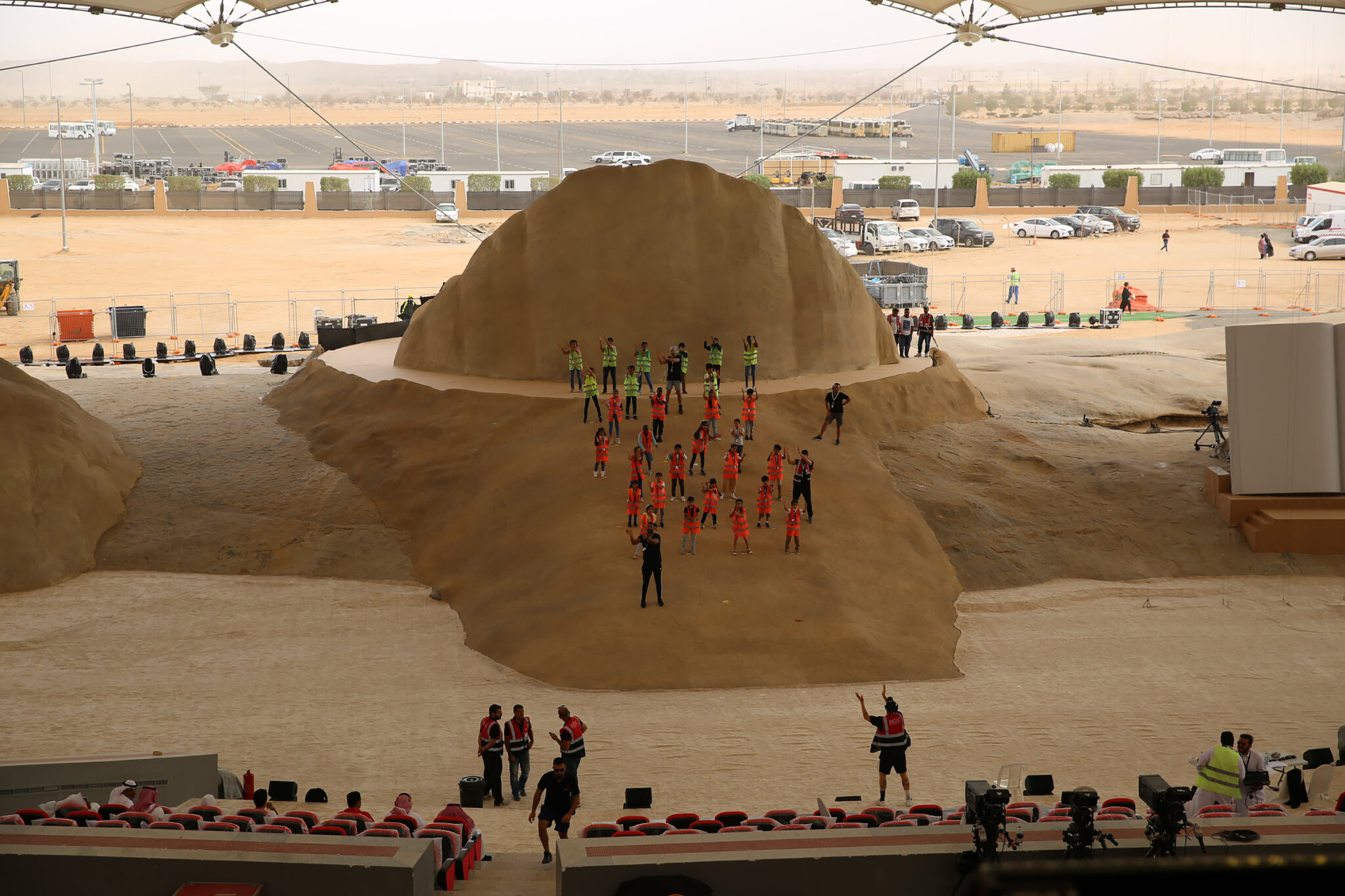 Aerial daytime view of a large rock-shaped stage structure set in open desert, with seating and tents arranged around it.