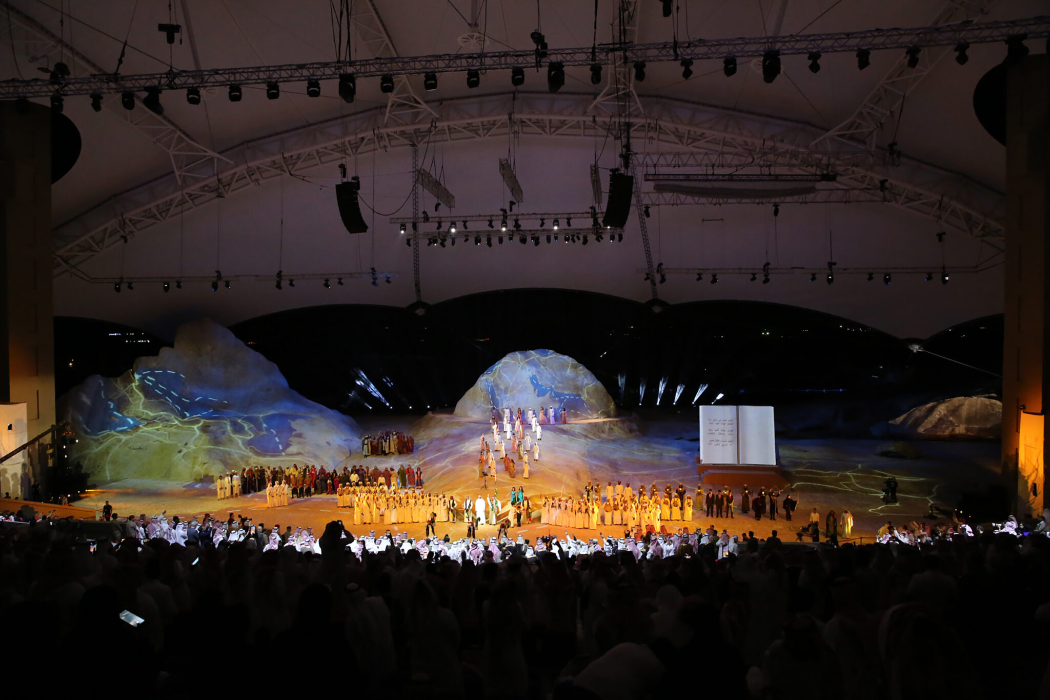 A wide empty stage built as a rocky outcrop under a peaked tent roof, lit in soft colour before the audience arrives.