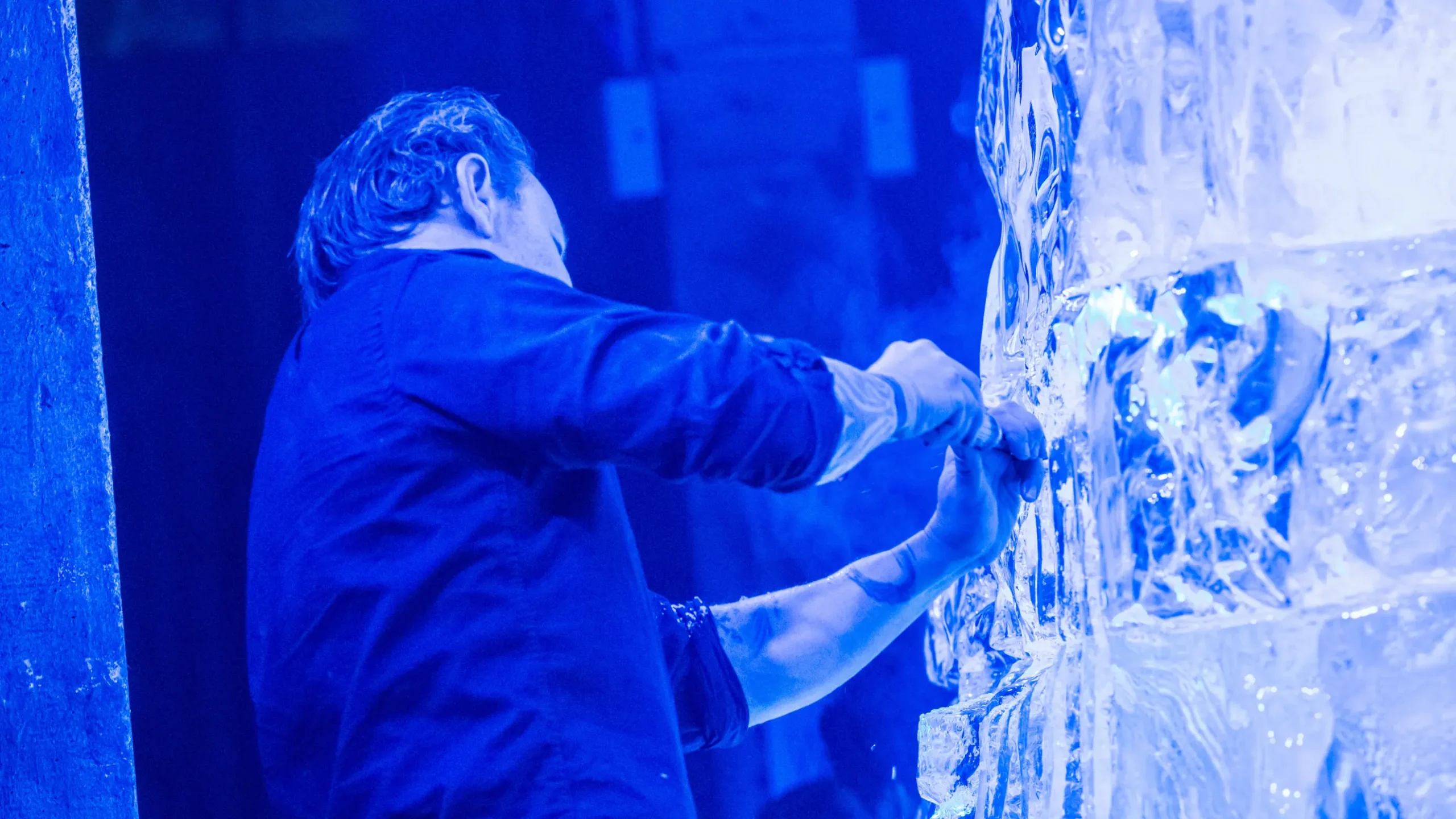 A person is carving an ice sculpture, illuminated by blue lighting. Battle Royal Studios