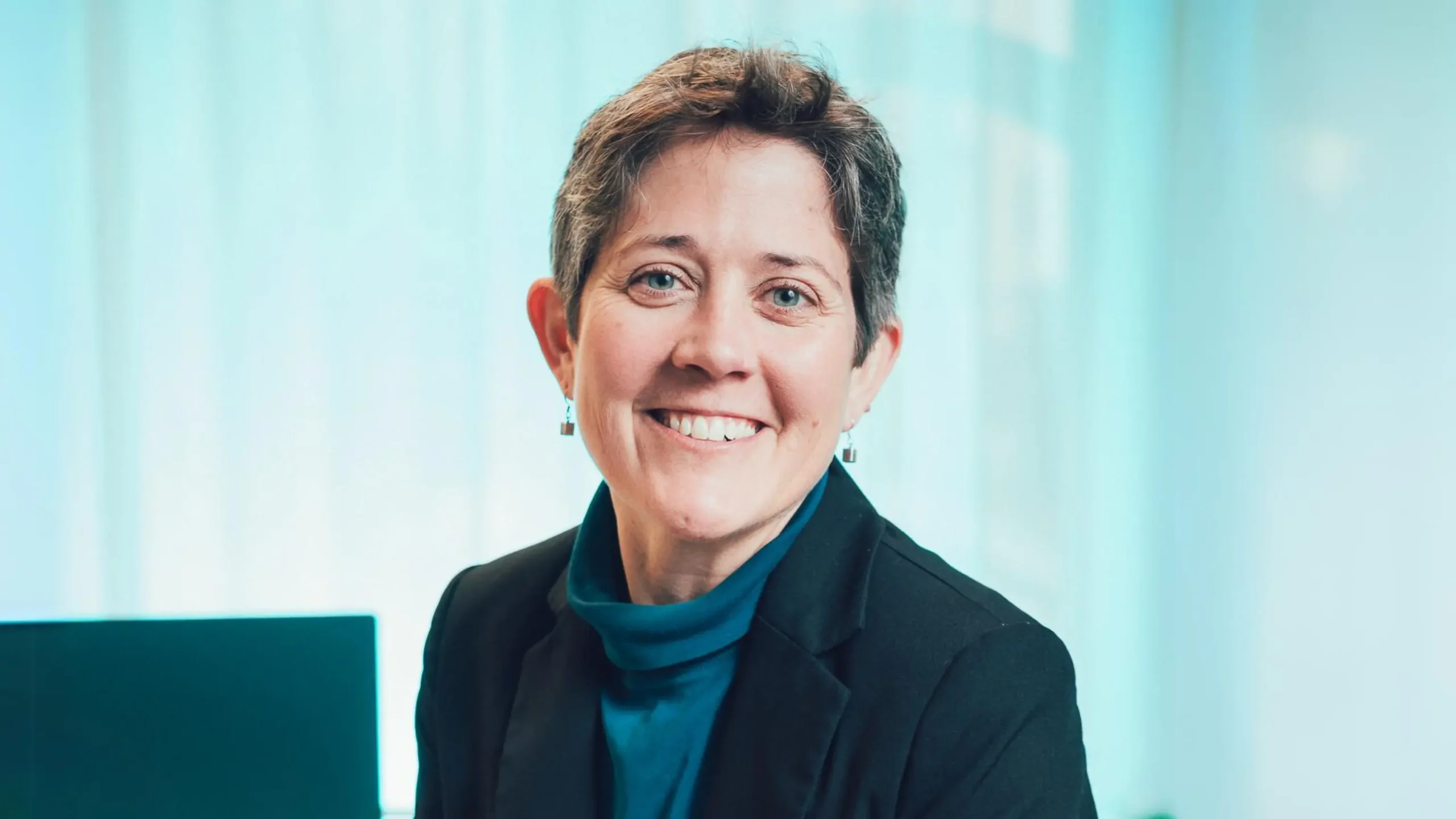A smiling woman with short hair in a blazer in a bright office