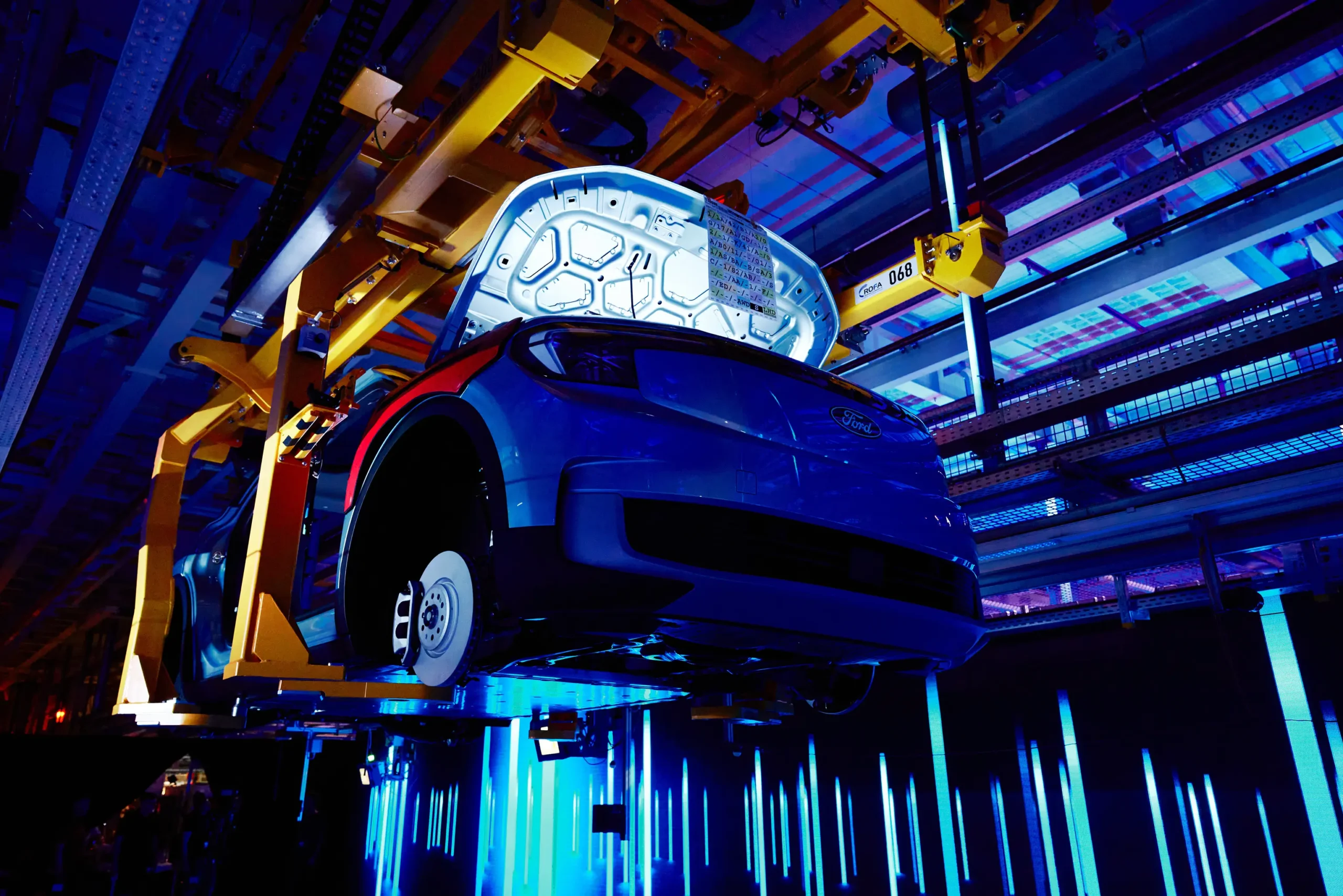 A car is suspended on a production line, illuminated with blue lighting, with the hood open, revealing its interior. Battle Royal Studios