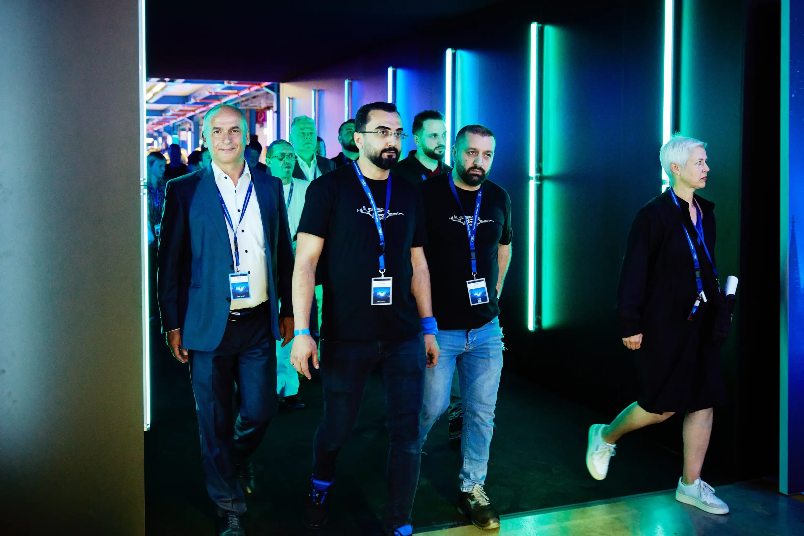 A group of people walk through a hallway lit by neon lights, with some wearing lanyards and badges. Battle Royal Studios