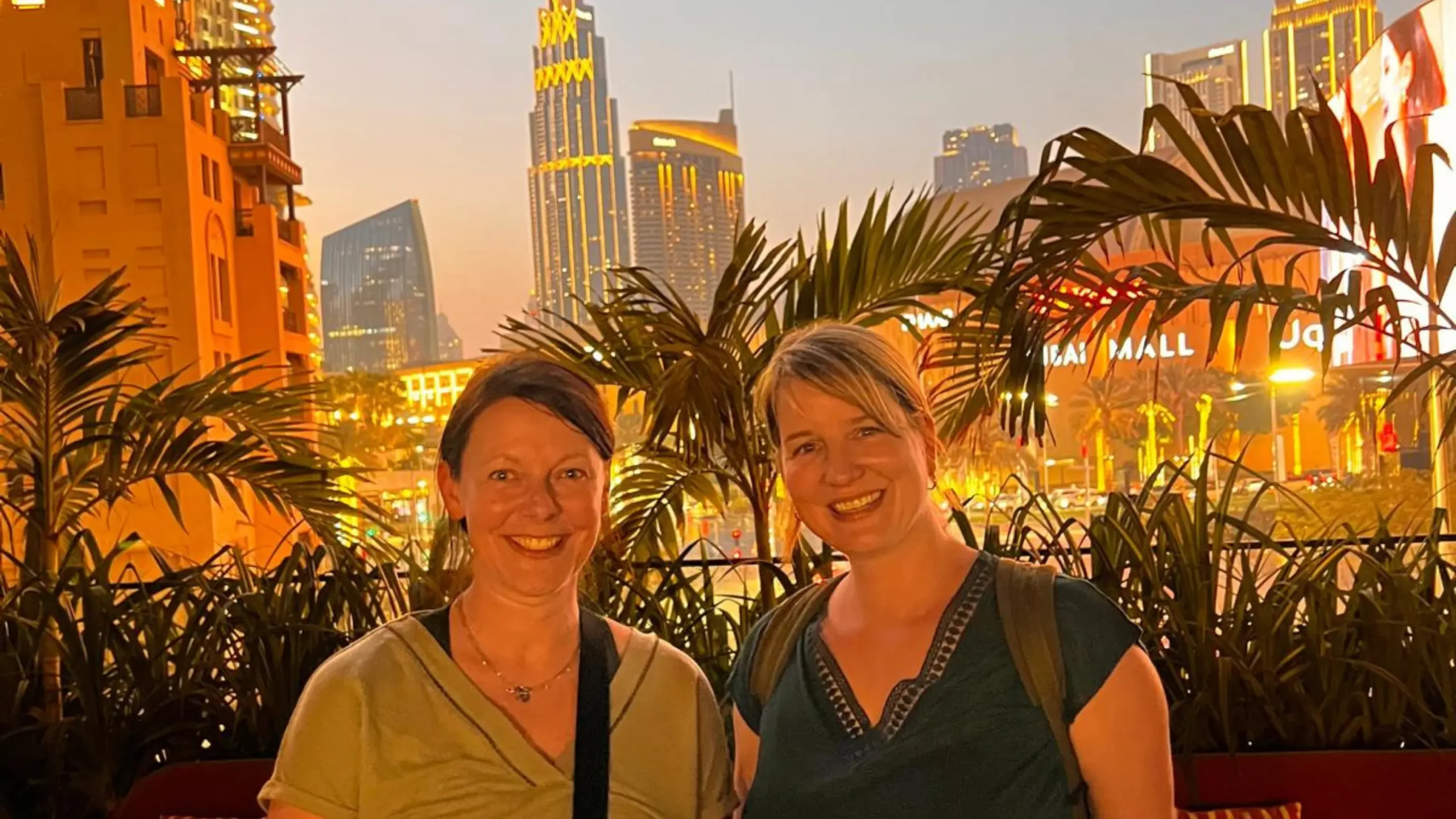 Sarah La Tragna and Judith Hoch smile while standing outdoors, with skyscrapers and city lights in the background at sunset. Battle Royal Studios