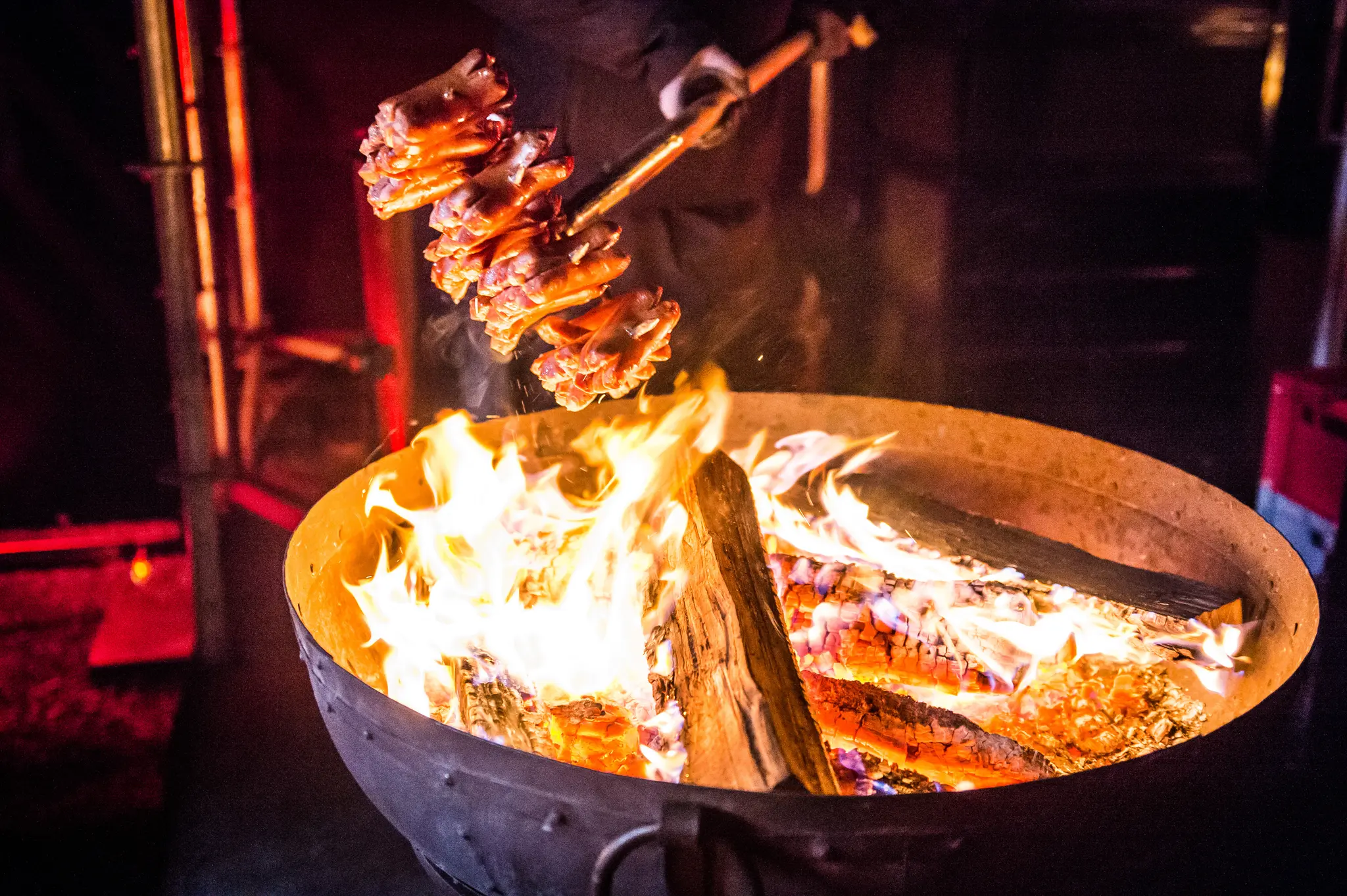 Close-up of skewered meat roasting over open flames in a fire bowl